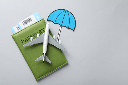 Travel insurance. Plane model, passport, paper umbrella and tickets on light grey background, flat lay. Space for textの写真素材