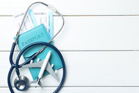 Medical tourism. Stethoscope, plane model, passport and flight tickets on white wooden table, flat lay. Space for textの写真素材