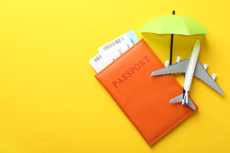 Travel insurance. Plane model, passport, small umbrella and tickets on yellow background, flat lay. Space for textの写真素材