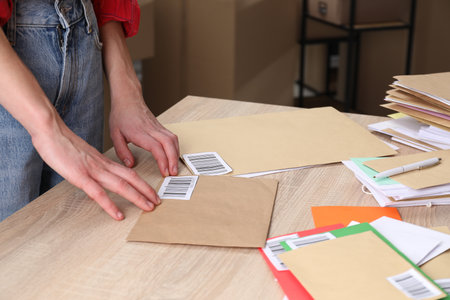 Woman putting barcodes onto envelopes at table in post office, closeupの写真素材