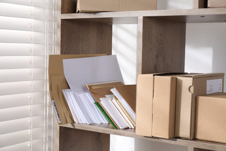 Different paper envelopes and parcels on wooden shelves in post office