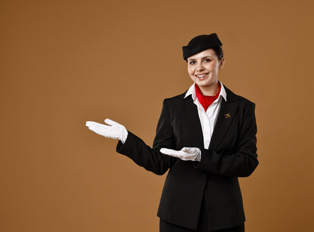 Smiling stewardess showing something on brown background. Space for textの写真素材