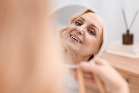 Smiling middle aged woman with round mirror at homeの写真素材