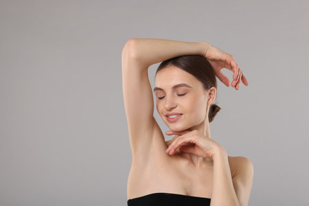 Young woman showing smooth skin after epilation on gray backgroundの写真素材