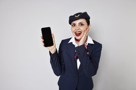 Excited stewardess with smartphone on grey background