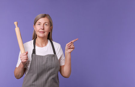 Woman with rolling pin pointing at something on violet backgroundの写真素材