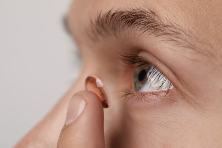 Man putting color contact lens in his eye on light background, closeupの写真素材