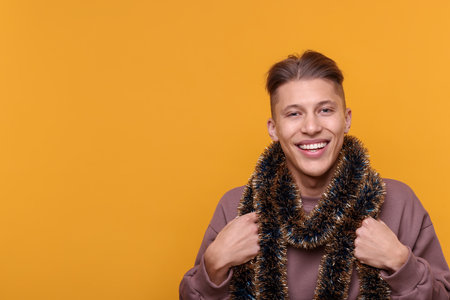 Happy young man with tinsel on orange background, space for textの写真素材