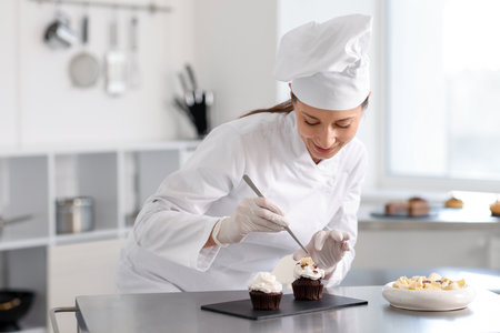 Confectioner decorating cupcake with piece of chocolate in kitchenの写真素材