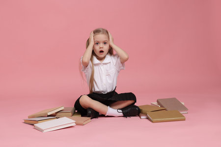 Emotional schoolgirl with books on pink background
