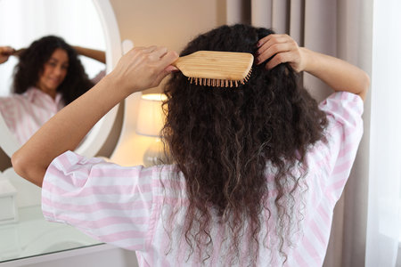 Woman brushing her curly hair near mirror at home, selective focusの写真素材
