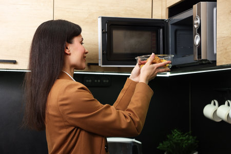Woman putting container with lunch into microwave indoorsの写真素材