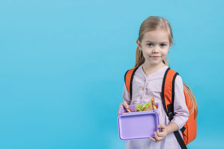 Cute little girl with lunch box on light blue background. Space for textの写真素材