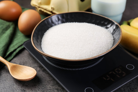 Digital kitchen scale with bowl of sugar and other products on grey table, closeupの写真素材