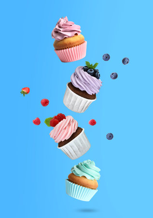 Yummy cupcakes with fresh berries falling on light blue background