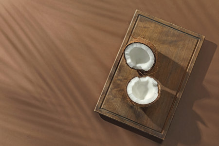 Fresh coconut and shadow cast by tropical palm on beige background, top view. Space for text