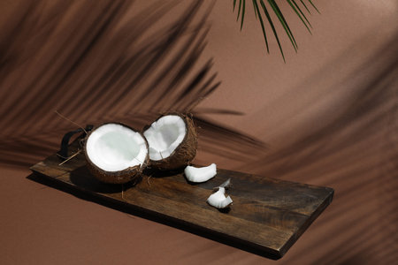 Fresh coconut and shadow cast by tropical palm on light brown background, closeup