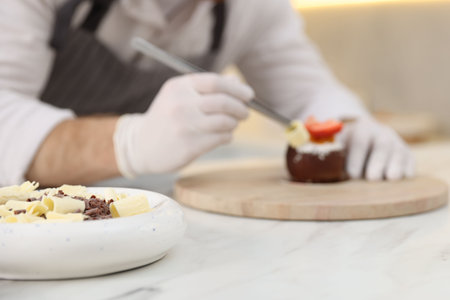 Confectioner decorating delicious dessert at white marble table in kitchen, focus on chocolate shavingsの写真素材