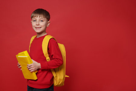 Cute schoolboy with backpack and books on red background, space for textの写真素材