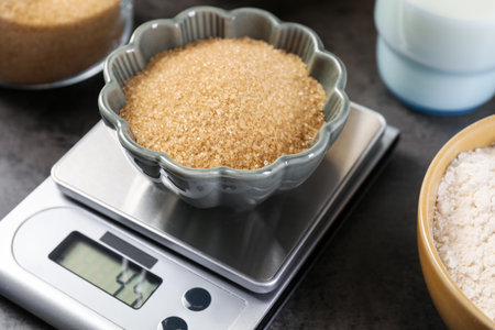 Digital kitchen scale with bowl of brown sugar and other products on grey table, closeupの写真素材