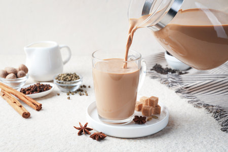 Pouring aromatic Masala tea in glass cup at white textured table, closeupの写真素材
