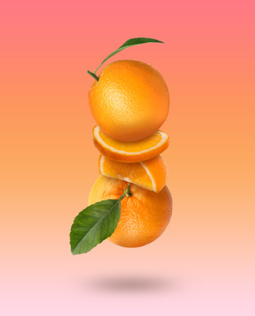 Fresh juicy oranges with green leaves falling on color gradient backgroundの写真素材