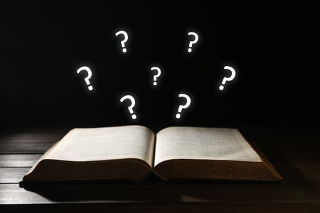 Question marks over open book on wooden table against black backgroundの写真素材