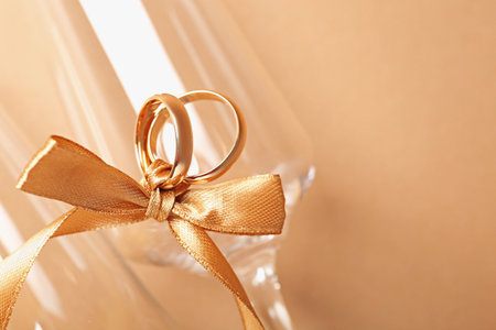 Wedding rings tied with ribbon and glasses on beige background, top view. Space for textの写真素材