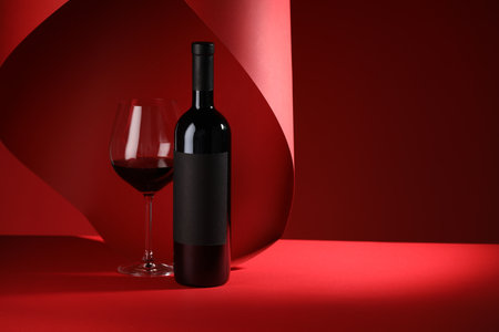 Bottle and glass of tasty wine on red background. Space for textの写真素材