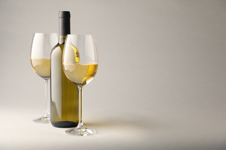 Tasty white wine in glasses and bottle on light grey background, space for textの写真素材