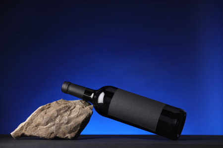 Bottle of wine and rock on black table against dark blue background, space for textの写真素材