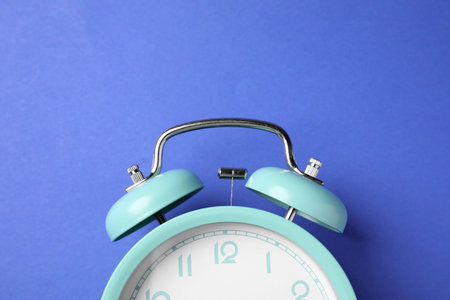 Turquoise alarm clock on blue background, top view