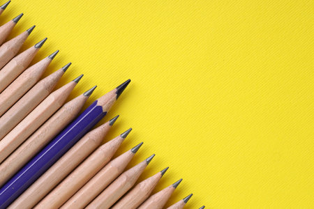 One blue pencil among graphite ones on yellow background, top view.の写真素材