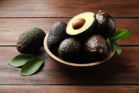 Fresh ripe avocados and leaves on wooden table, closeup