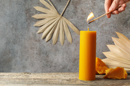 Woman lighting beeswax candle at wooden table, closeup. Space for textの写真素材