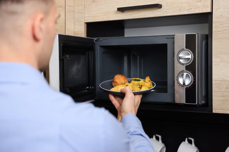 Man putting plate with lunch into microwave in kitchen, closeupの写真素材