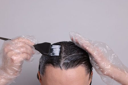 Woman dyeing her hair on gray background, closeup