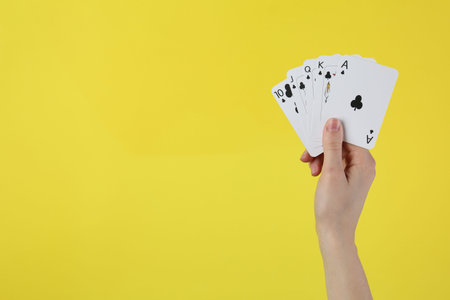 Hand with playing cards against yellow background, closeup. Space for text