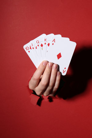 Woman showing playing cards through hole in red paper, closeup