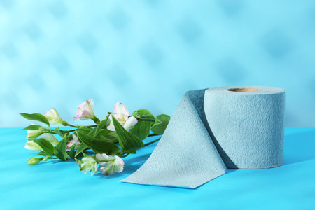 Light blue toilet paper roll and beautiful flowers on color backgroundの写真素材