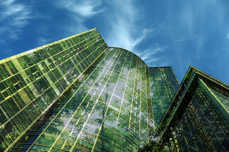 Modern skyscrapers and lush trees against blue sky, double exposure. Low angle viewの写真素材