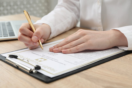 Doctor filling out health insurance policy at wooden table in clinic, closeupの写真素材