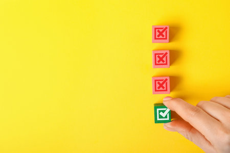 Approved. Woman choosing cube with check mark among other ones with crosses on yellow background, top viewの写真素材