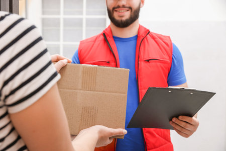 Smiling courier with clipboard giving parcel to receiver indoors, closeupの写真素材