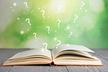 Question marks flying out from open book on grey wooden table against blurred green backgroundの写真素材