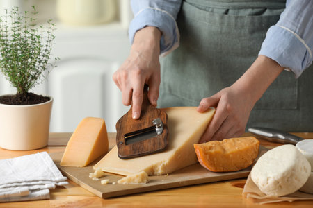 Woman cutting delicious cheese with slicer at wooden table indoors, closeupの写真素材