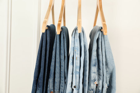 Many stylish jeans hanging against white wallの写真素材