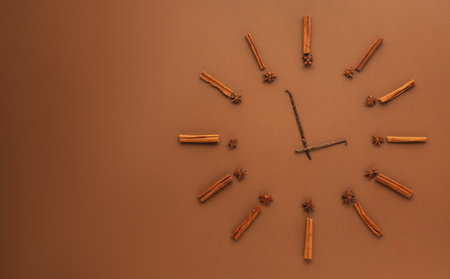 Cinnamon sticks, anise stars and vanilla pods representing clock on brown background, flat lay. Space for textの写真素材