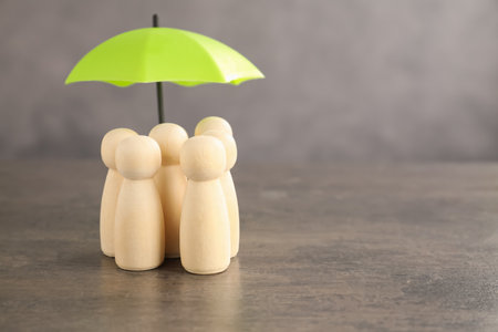 Human figures under umbrella on grey table, space for text. Insurance conceptの写真素材