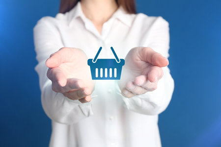 Online store. Woman holding virtual shopping basket icon on blue background, closeupの写真素材